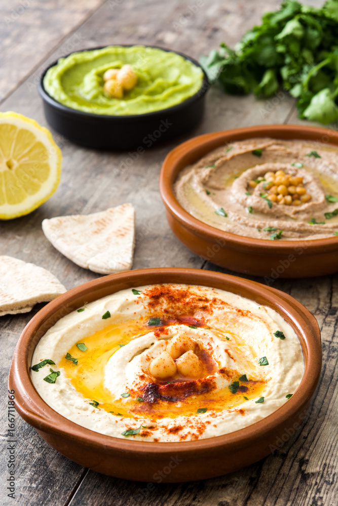 Different hummus bowls. Chickpea hummus, avocado hummus and lentils hummus on wooden table
Different hummus bowls. Chickpea hummus, avocado hummus and lentils hummus on wooden table
