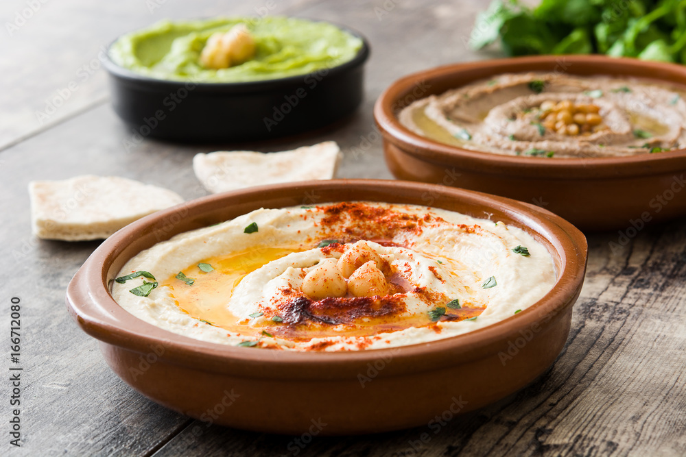 Different hummus bowls. Chickpea hummus, avocado hummus and lentils hummus on wooden table

