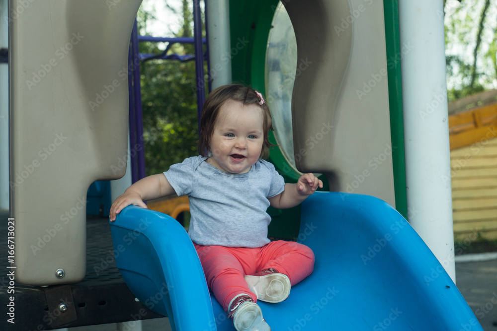 Happy little baby girl rolling down the hill on the playground Happy little baby girl rolling down the hill on the playground