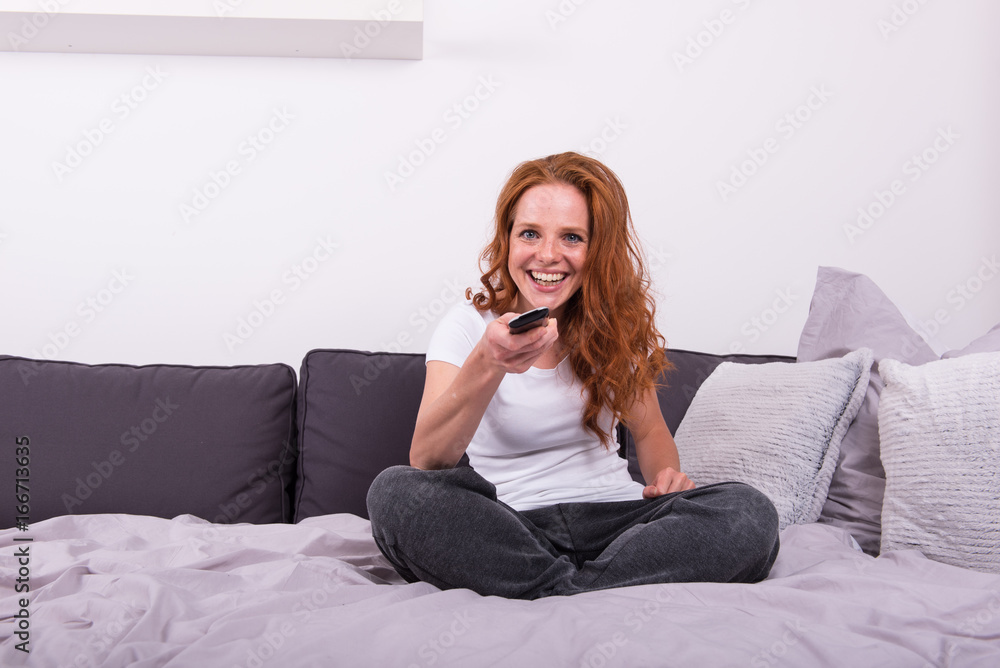 junge rothaarige Frau mit der Fernbedienung in der Hand sieht Fernsehen junge rothaarige Frau mit der Fernbedienung in der Hand sieht Fernsehen