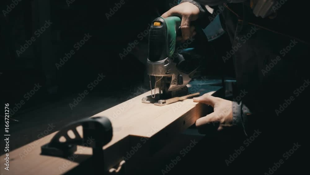 Worker carpentry workshop, using the jigsaw , cut the block, assembly of garden furniture, uses professional tools, lowlight Worker carpentry workshop, using the jigsaw , cut the block, assembly of garden furniture, uses professional tools, lowlight