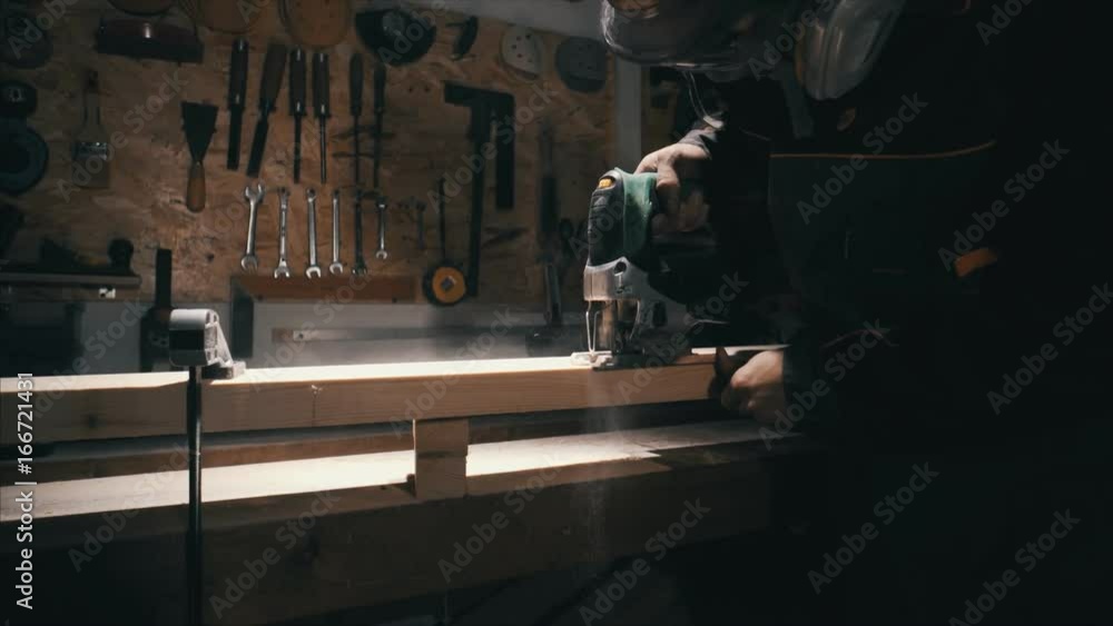 Joiner works with an electric jigsaw, worker make a part of furniture, lowlight Joiner works with an electric jigsaw, worker make a part of furniture, lowlight
