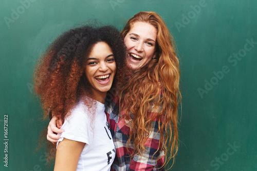 Portrait of two girlfriends laughing against of green background photo