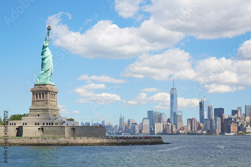 Statue of Liberty island and New York city skyline in a sunny day, white clouds © andersphoto