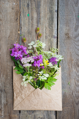Wild field flowers in craft paper envelope over wooden background