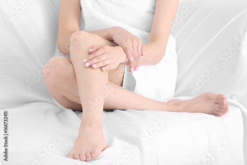 Epilation concept. Young woman sitting on sofa, closeup view of female legs