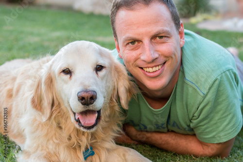Man with his Golden Retriever dog laying on grass outdoors looking at camera smiling.