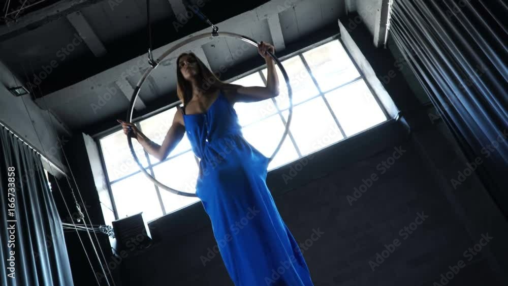 Beautiful girl in long dress is moving in the aerial hoop at window background Beautiful girl in long dress is moving in the aerial hoop at window background