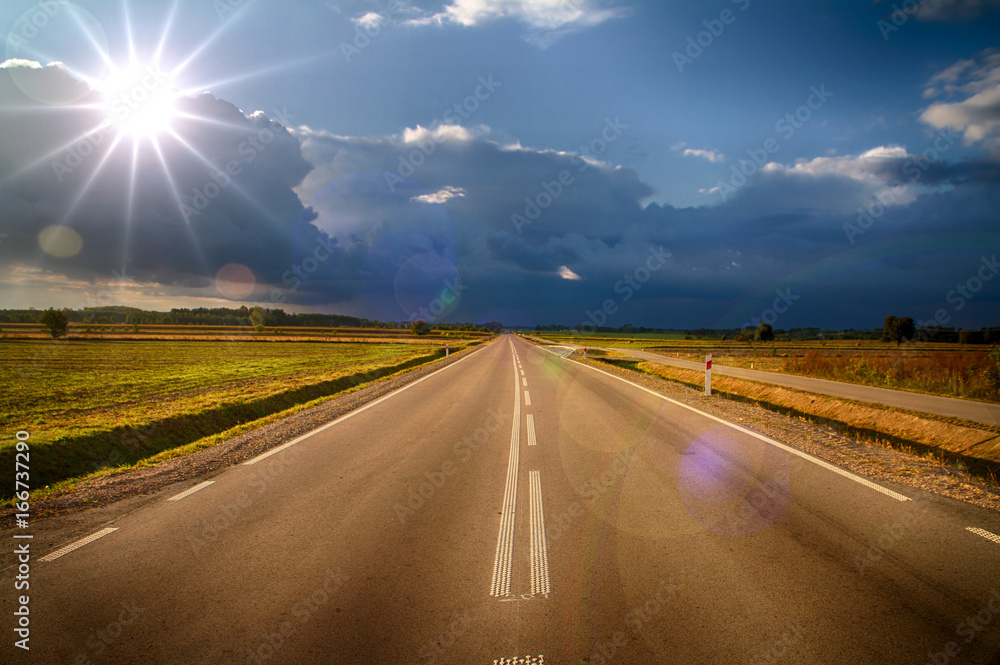 Asphalt road running towards the horizon illuminated from the front of the sun