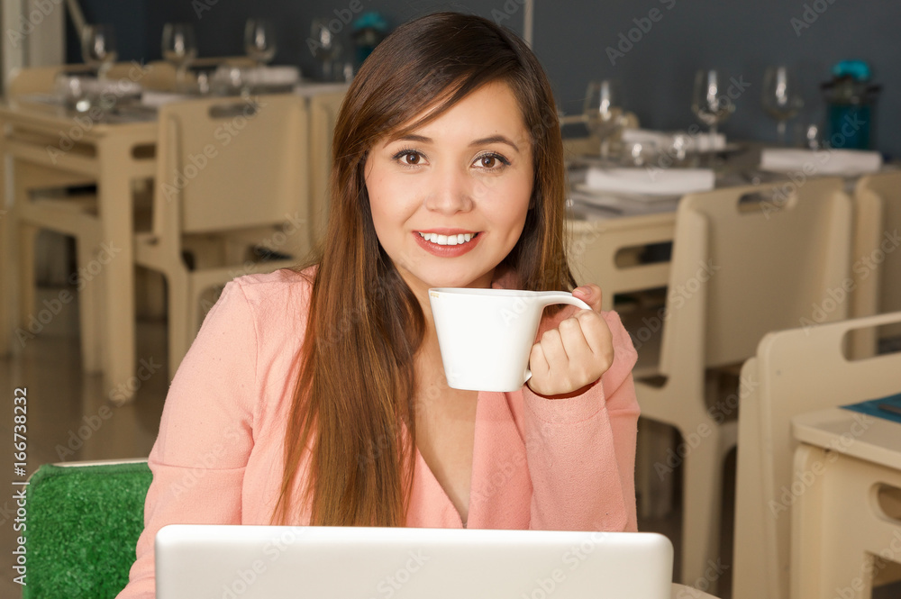 Close up of a young beautiful smiling businesswoman working and holding with one hand a cup of coffe. Business concept Close up of a young beautiful smiling businesswoman working and holding with one hand a cup of coffe. Business concept