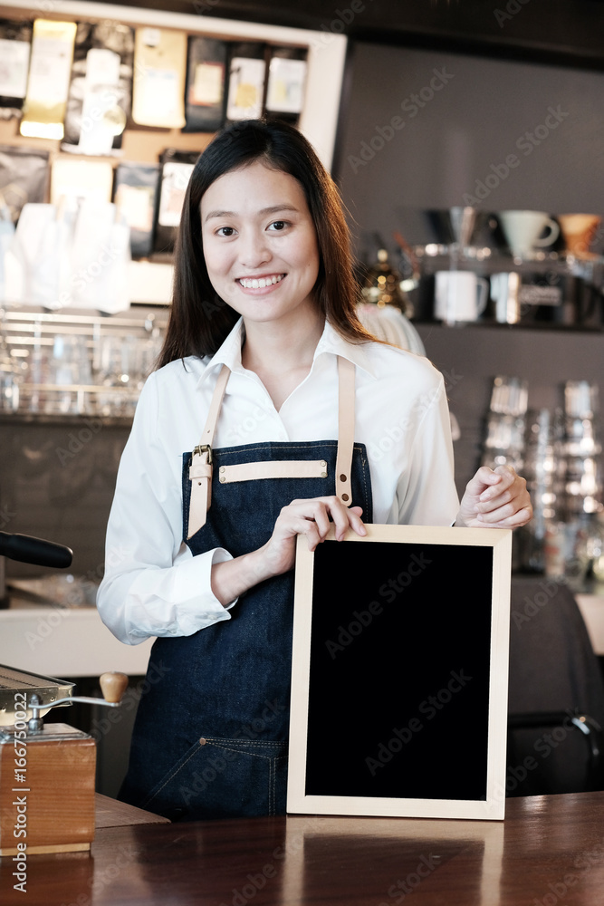 Young asian women Barista holding blank chalkboard with smiling face at cafe counter background, small business owner, food and drink industry concept