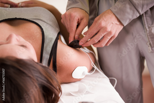 Close-up of a personal trainer hand putting an electrostimulator electrodes in the arm and shoulder of a female deportist  lying on her back