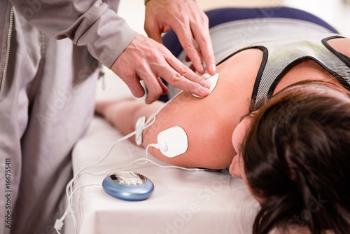 Close-up of a personal trainer hand putting an electrostimulator electrodes in the arm of a female deportist, upside down on a bed
