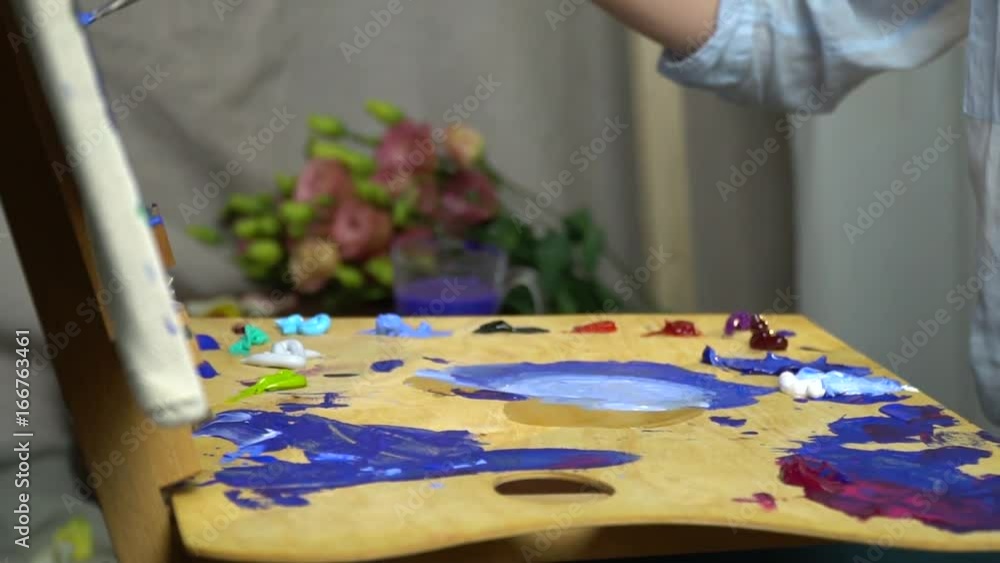 Female hands mix colors on the palette and paint on the canvas side view, a bit slow motion Female hands mix colors on the palette and paint on the canvas side view, a bit slow motion