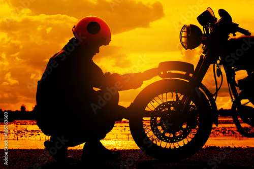 Silhouette of biker man with his motorbike beside the natural lake and beautiful, enjoying freedom and active lifestyle, having fun on a bikers tour.sunset background and sky.