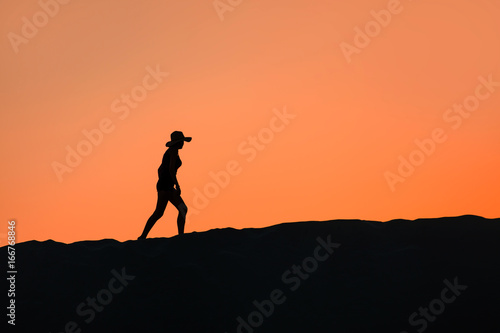 Silhouette of woman walking on the sand hill at sunset - Patara, Turkey