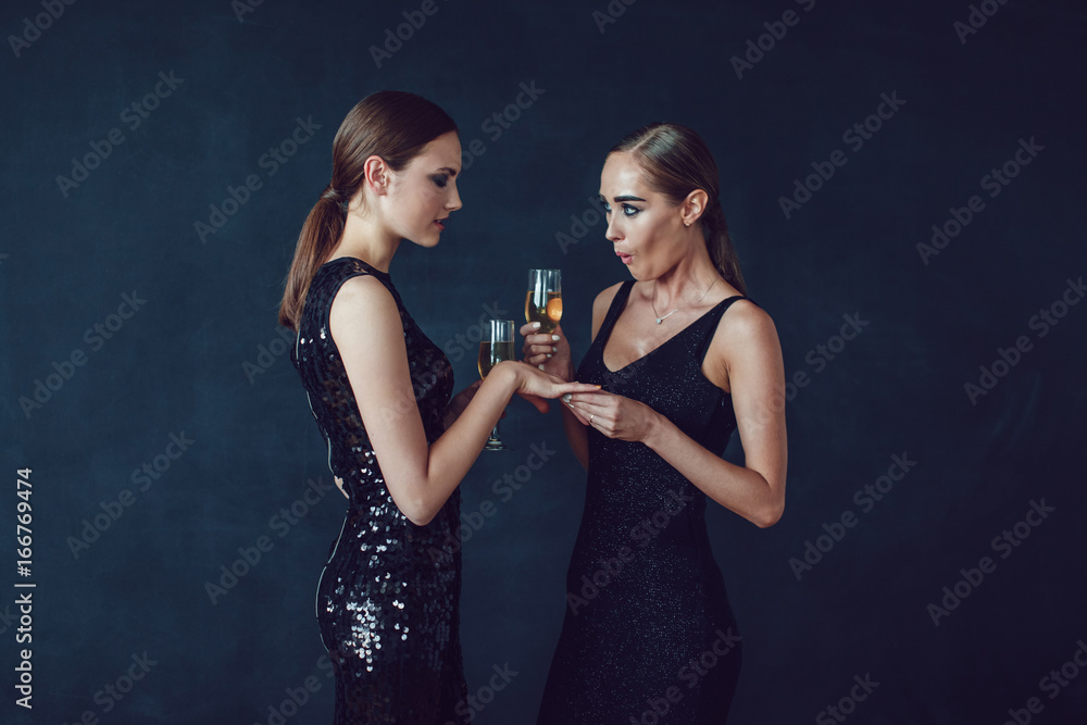 Attractive women in cocktail dresses are holding glasses of champagne, talking and smiling. Attractive women in cocktail dresses are holding glasses of champagne, talking and smiling.