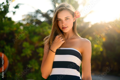 Spa wellness beach beauty woman relaxing andlooking at camera on beach. Beautiful serene and peaceful young female model on holiday travel resort enjoting vacation. Flower in braided hair photo