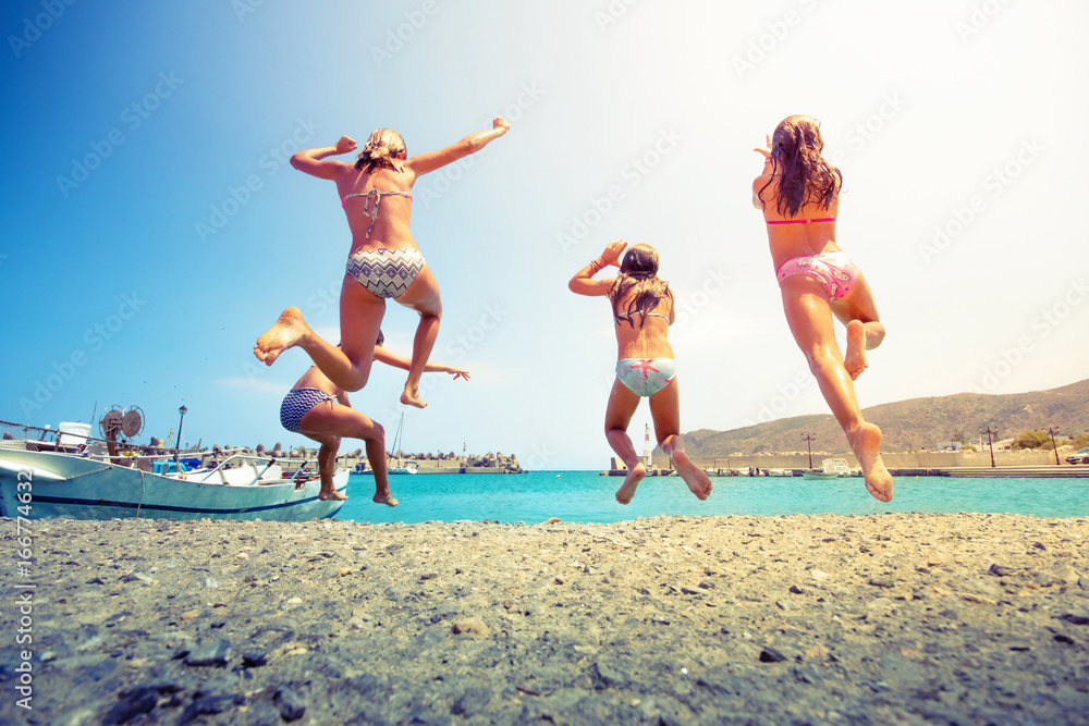 Group of friends jumping to the sea from the pier, happy beach holidays, Crete, Greece Group of friends jumping to the sea from the pier, happy beach holidays, Crete, Greece