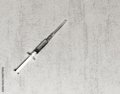 A disposable medical syringe with an injection needle on a gray background with space for text. black and white photo