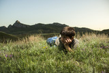 Boy lying in grass at backdrop of the mountains