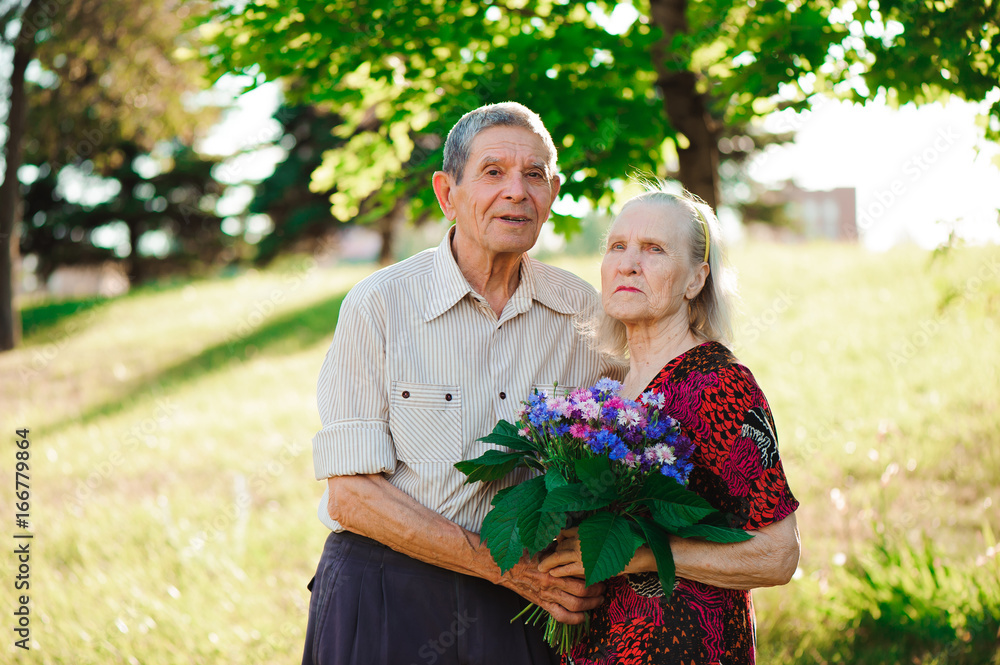 An elderly man of 80 years old gives flowers to his wife in a summer park.