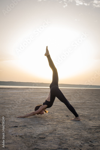 young fit woman training yoga poses in desert during the sunset or sunrise, female in black sportswear do stretching exercises 