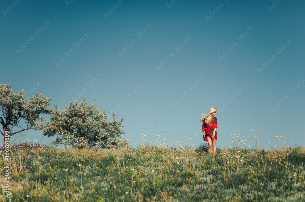 Blond girl in a red dress in the nature