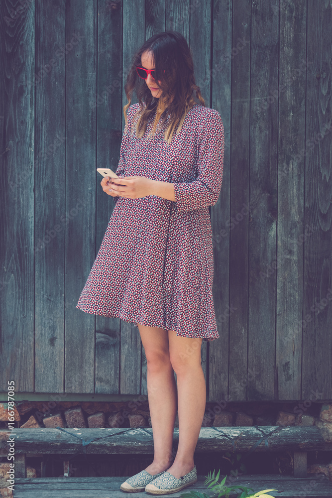 Obraz premium Young female using smartphone against wooden wall