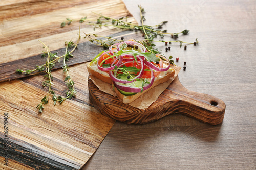 Wooden board with delicious toast and vegetables on table