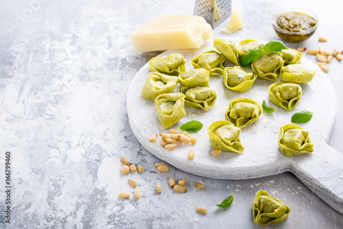 Homemade raw Italian tortelloni and ingredients for green pesto on marble cutting board on light gray background. Healthy food concept. Selective focus. Copy space. photo