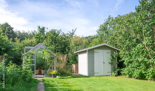 Obraz na płótnie Greenhouse and shed in green  lush garden