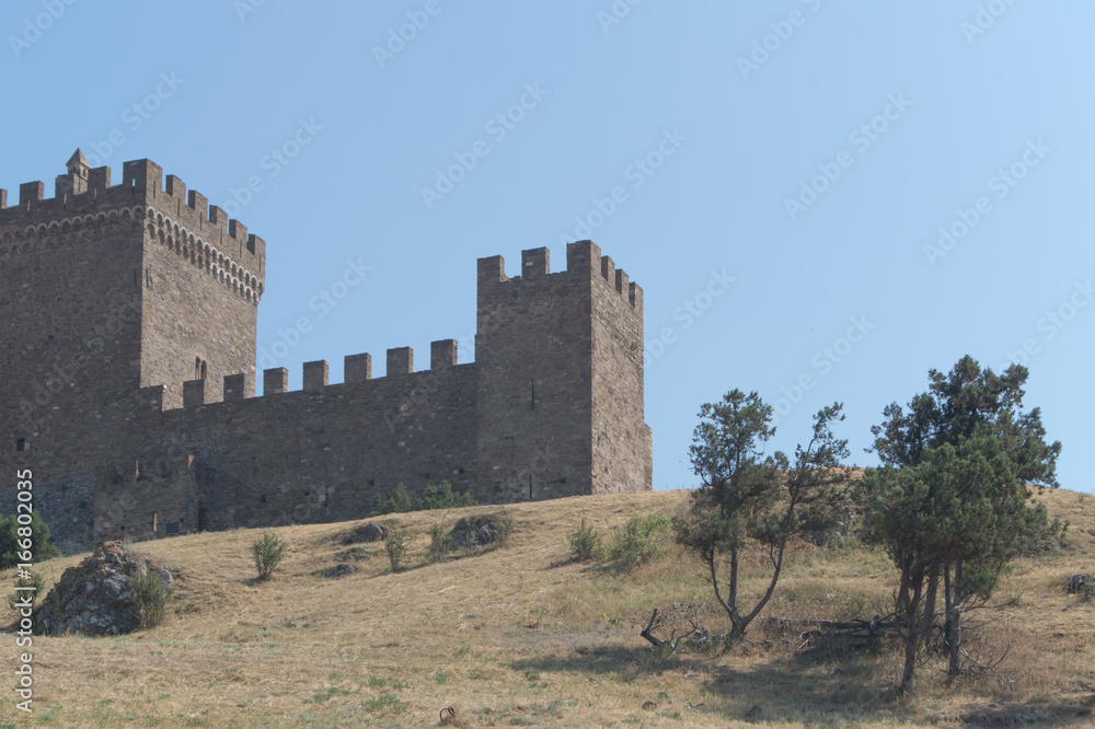Old brown stone fortress with battlements on the background of the blue sky. Sudak, Crimea Old brown stone fortress with battlements on the background of the blue sky. Sudak, Crimea
