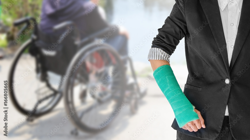 Female patient wearing black suit with green cast on arm isolated on blurred background patient sitting on wheelchair, body injury concept Female patient wearing black suit with green cast on arm isolated on blurred background patient sitting on wheelchair, body injury concept