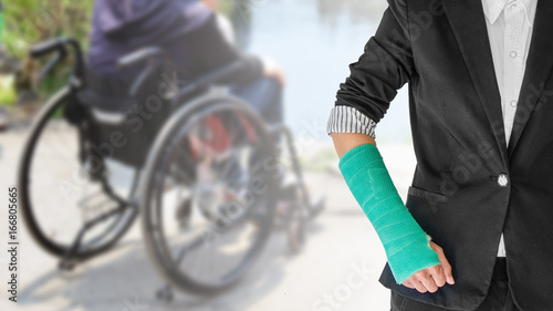 Female patient wearing black suit with green cast on arm isolated on blurred background patient sitting on wheelchair, body injury concept
