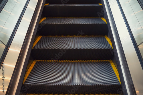 Empty escalator or moving stair. Also called stairway or staircase. Modern architecture design with step, glass for lift people up floor building i.e. shopping mall, airport, metro and subway station.