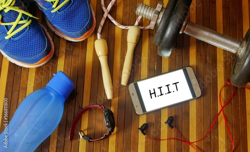 Fitness, healthy and active lifestyles concept. Dumbbells, sport shoes, smart phone with earphone, skipping rope and water bottle gym floor with word H.I.I.T (high intensity interval training)