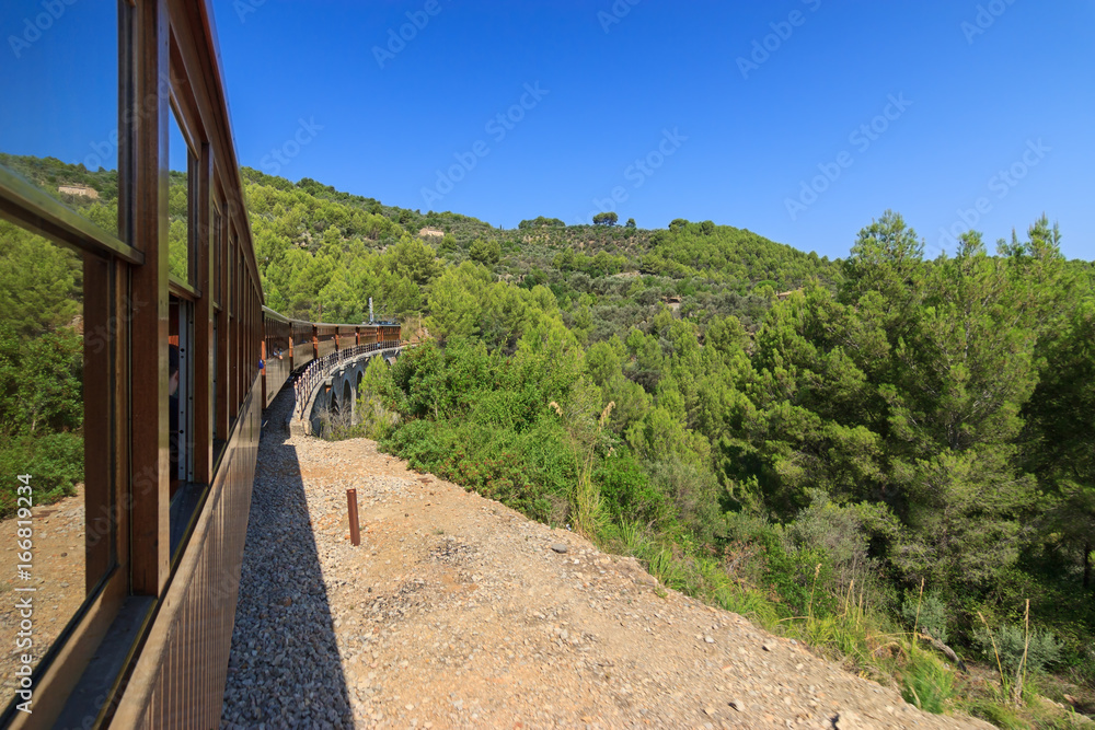 View aboard the Soller train crossing a bridge between a pine forest in Serra de Tramuntana mountains, Majorca Balearic Islands