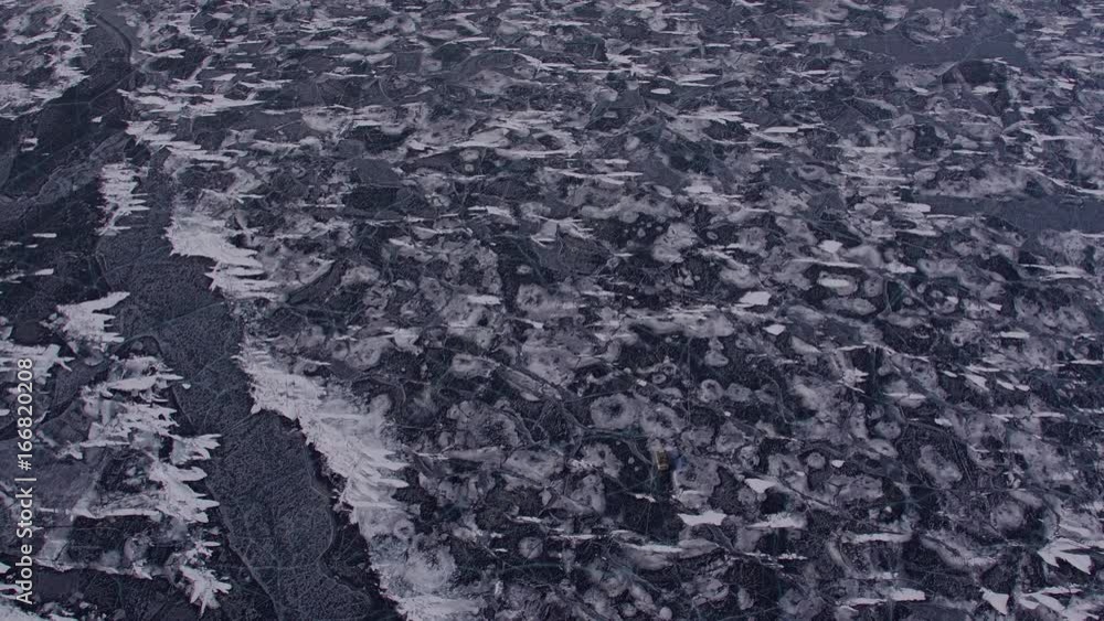 Frozen lake Baikal covered with snow and ice. Cars are driving over the ice. Aerial view. Flying around 4k