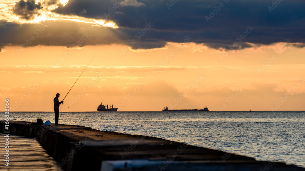 Fototapeta premium people enjoying sunset on the breakwater in the sea with lighthouse
