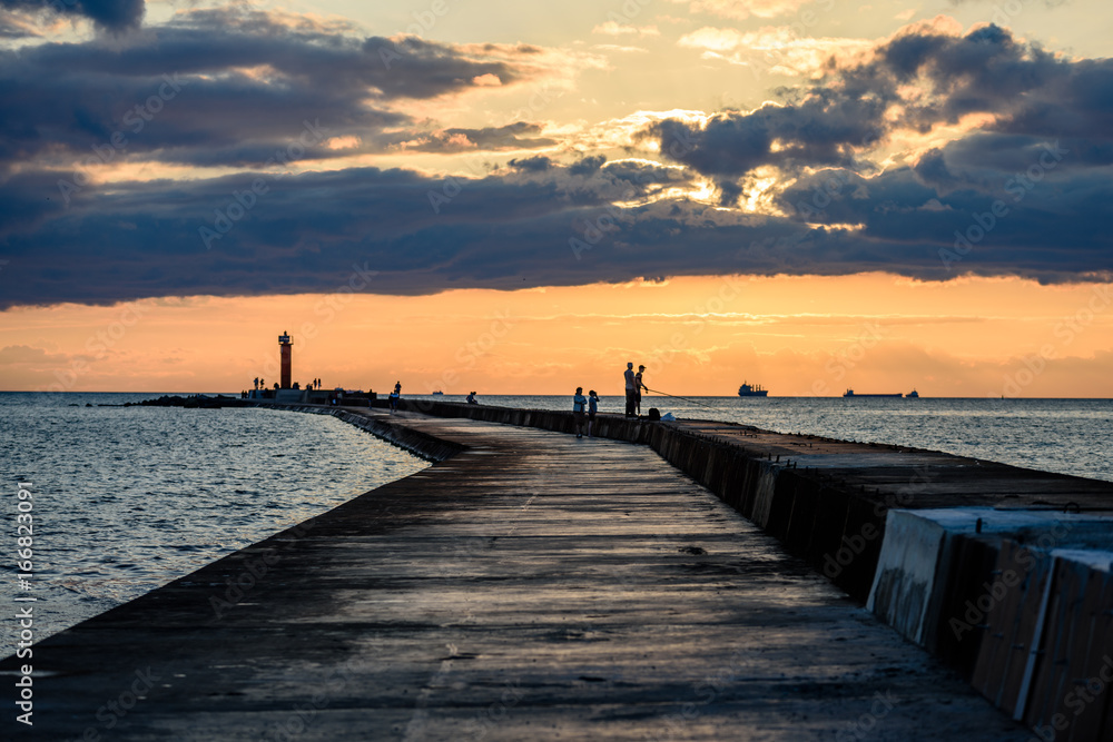 people enjoying sunset on the breakwater in the sea with lighthouse