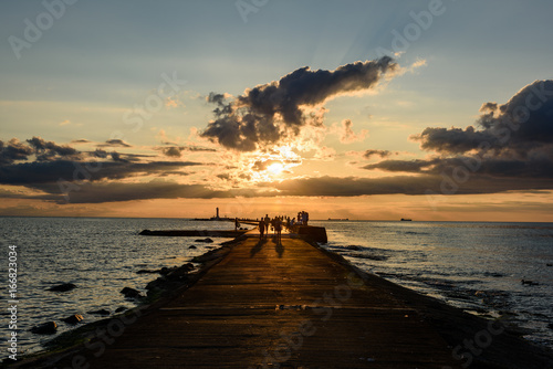 people enjoying sunset on the breakwater in the sea with lighthouse