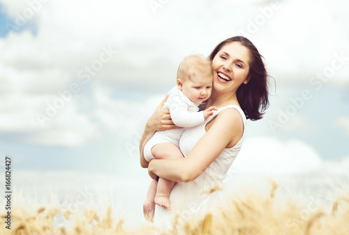 Beautiful woman holding baby. Mother and son walking in a meadow at summer.