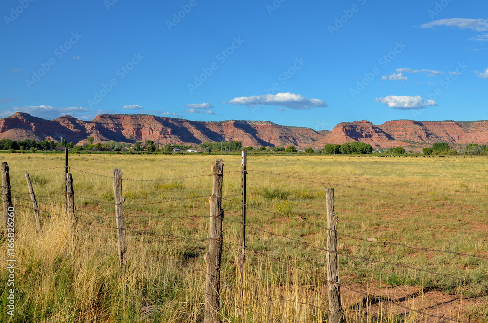 green pasture and red rocks behind barbed wire fence  at sunset 
Kanab, Kane County, Utah