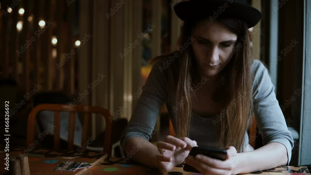 Beautiful stylish woman in hat sitting at the table and using smartphone technology for browsing the Internet. Beautiful stylish woman in hat sitting at the table and using smartphone technology for browsing the Internet.