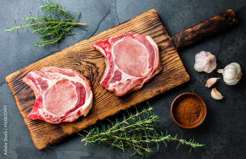 Raw pork cutlet chop for fry on pan with herbs, garlic on wooden boards, slate gray background photo
