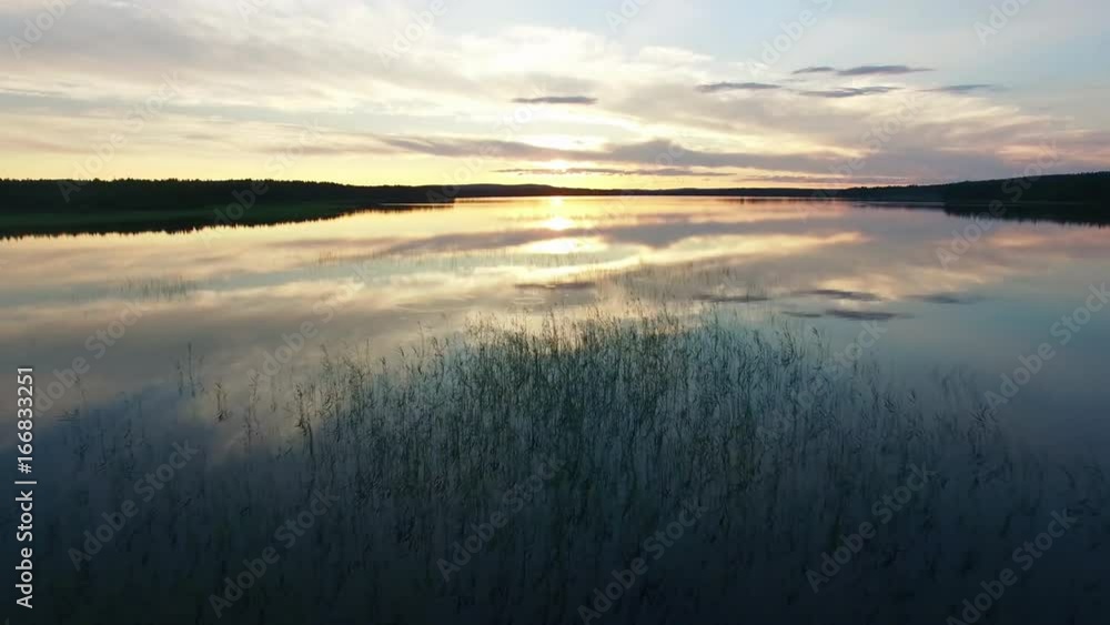 Flying over lake at sunset. Aerial shot of calm lake with beautiful reflections in the water Flying over lake at sunset. Aerial shot of calm lake with beautiful reflections in the water