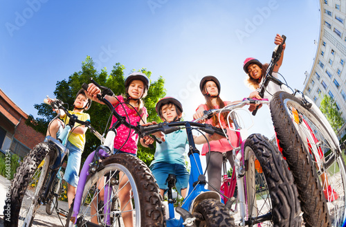 Happy little bike riders standing against blue sky