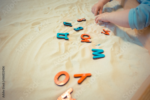 a child in a sandbox lays out the letters of the Russian alphabet educational activities for kids