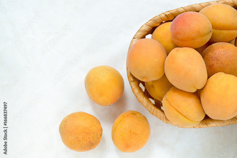 Ripe apricots in a wicker wooden plate and a few apricots nearby. Light background, top view. Copy Space Ripe apricots in a wicker wooden plate and a few apricots nearby. Light background, top view. Copy Space